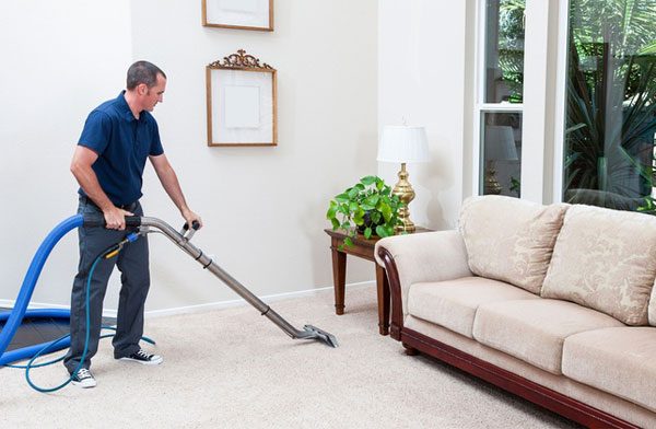 This image shows a man using a vacuum to clean a carpet. The carpet being cleaned is color white.